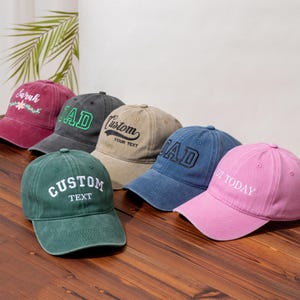 Può includere: Una collezione di sei cappellini da baseball in vari colori, tra cui bordeaux, grigio antracite, beige, blu, verde e rosa. Ogni cappellino presenta testo o disegni ricamati, come Sarah, DAD, Custom Your Text e NOT TODAY, con visiera curva.