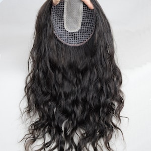 May include: A dark brown hair topper with long, wavy hair. The base is a fine, breathable mesh with a U-shaped design. The hairpiece is held up by a hand against a white background. This hair topper is designed to add volume and coverage.