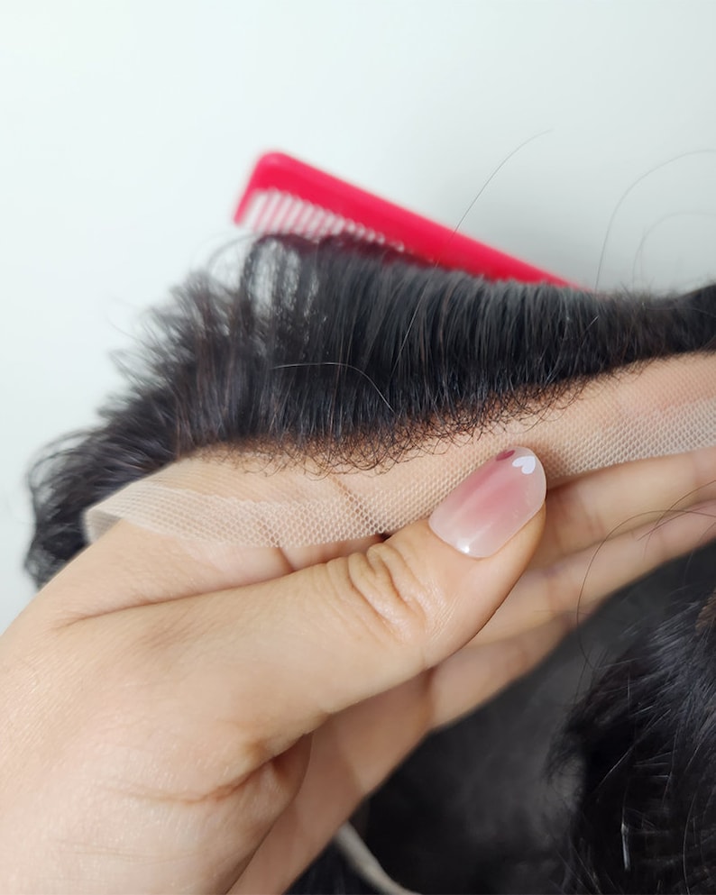Puede incluir: Primer plano de una peluca negra con un frente de encaje. La peluca se sostiene en una mano con esmalte de u&ntilde;as rosa y un dise&ntilde;o de coraz&oacute;n blanco.