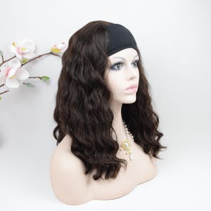 May include: A dark brown wavy wig featuring a black headband base, displayed on a mannequin head. The hair has a natural wave pattern and falls to shoulder length. A white pearl necklace with a gold-toned pendant is visible around the neck.