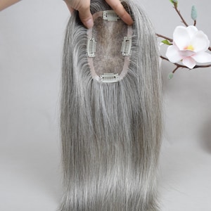 May include: A gray hair topper with a lace base and multiple clips for secure attachment. The hair is straight and falls to a medium length. The topper is designed to add volume and coverage to thinning hair.