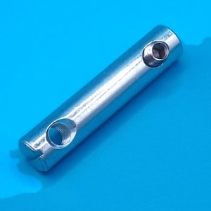 Könnte beinhalten: Ein zylindrischer silberfarbener Metall-Verbindungsbolzen mit glatter Außenfläche, einer seitlichen Gewindebohrung und einem versenkten Innensechskant-Schraubenkopf, der sich nahe einem Ende des Bauteils für Befestigungszwecke befindet.