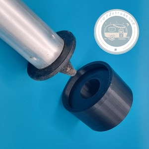 Op de afbeelding: Een zwart cilindrisch object met een gat in het midden, naast een zilveren metalen buis met een zwarte rubberen fitting. De achtergrond is effen blauw. Een sticker met een kampeerwagen illustratie en de tekst "rdy2xtrude.com" staat rechtsboven.