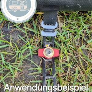 Könnte beinhalten: Ein schwarzes Band mit einer roten und goldenen Schnalle, befestigt an einer grauen Schlaufe. Das Band ist mit "Anwendungsbeispiel" beschriftet, was "Anwendungsbeispiel" bedeutet.