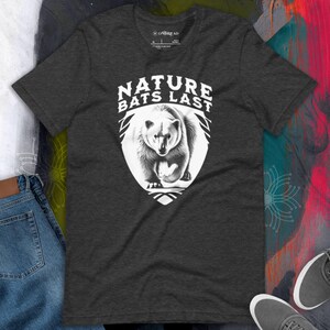 May include: A dark grey t-shirt featuring a white graphic of a polar bear and the text "Nature Bats Last".
