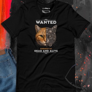 May include: Black t-shirt featuring a split image of a cat's face, half organic and half mechanical, with the word "WANTED" above and "SCHRÖDINGER'S CAT DEAD AND ALIVE" below. The design is centered on the shirt.