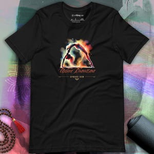 Peut inclure: T-shirt noir avec une illustration aquarelle d'une personne pratiquant la posture de yoga Upward Bow. Le texte "Urdhva Dhanurasana" et "Upward Bow" sont imprimés sous l'illustration.