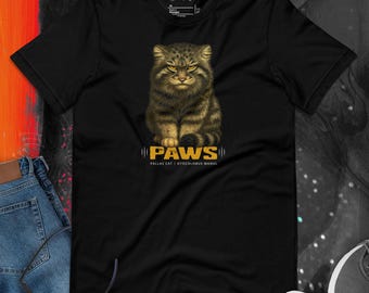 May include: Black t-shirt featuring a detailed illustration of a Pallas's cat with the word "PAWS" in gold lettering. The text "Pallas Cat | Otocolobus Manul" is below the word "PAWS". The shirt has a crew neck and short sleeves.