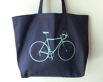 May include: A navy blue tote bag with a light blue bicycle design printed on the front. The bag has two long handles.