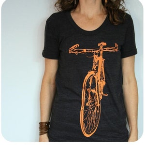 Könnte beinhalten: Ein dunkelgraues T-Shirt mit einem orangefarbenen Fahrrad-Motiv auf der Vorderseite.