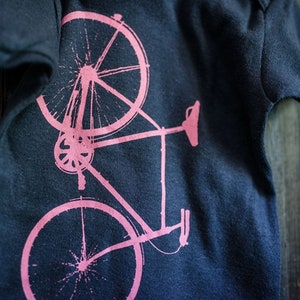 May include: A pink bicycle silhouette printed on a dark blue t-shirt.