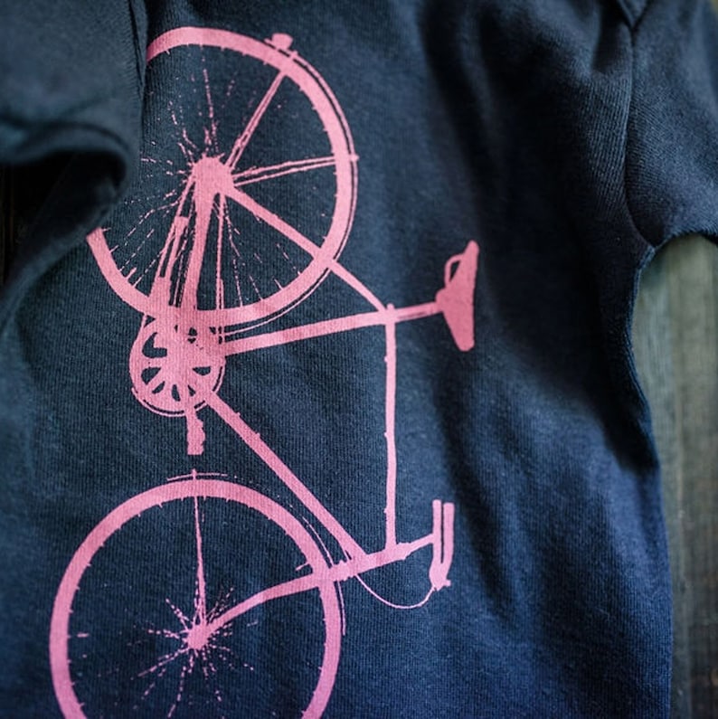 May include: A pink bicycle silhouette printed on a dark blue t-shirt.