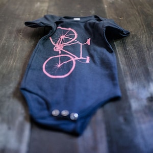 May include: A dark blue baby onesie with a pink bicycle graphic printed on the front.