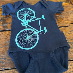 May include: A navy blue baby onesie with a teal bicycle graphic printed on the front.