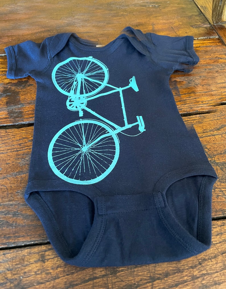 May include: A navy blue baby onesie with a teal bicycle graphic printed on the front.