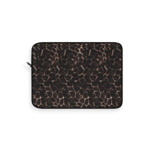 May include: A rectangular laptop sleeve with a brown and black giraffe print pattern. The sleeve has a black zipper closure on the left side. The pattern is a repeating design of irregular shapes.