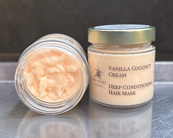 Può includere: Due barattoli di vetro contenenti una maschera per capelli color pesca pallido. Un barattolo è aperto e mostra la consistenza densa e cremosa del prodotto. L'altro barattolo è chiuso con un coperchio dorato e un'etichetta con scritto Vanilla Coconut Cream Deep Conditioning Hair Mask.