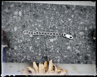 May include: A silver chain with a clasp, photographed on a speckled gray surface.