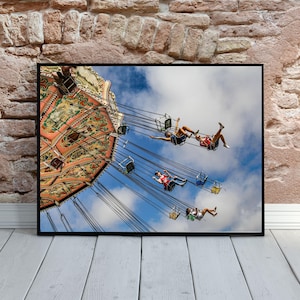 May include: A colorful carousel with people riding on swings against a blue sky with white clouds. The carousel is decorated with intricate designs and patterns.