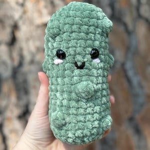 May include: A green crocheted plush toy shaped like a cactus with a smiling face and black eyes.