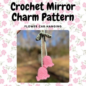 May include: Crochet flower car hanging charm pattern. Two pink crocheted flowers with green stems hang from a string. "Flower Car Hanging" is written in white text on a pink floral background.