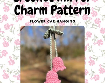 May include: Crochet flower car hanging charm pattern. Two pink crocheted flowers with green stems hang from a string. "Flower Car Hanging" is written in white text on a pink floral background.