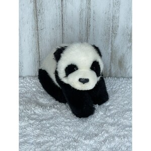 May include: A black and white plush panda bear toy with a soft, furry texture. The panda is lying down with its head tilted slightly to the side. It has black eyes, a black nose, and black paws.