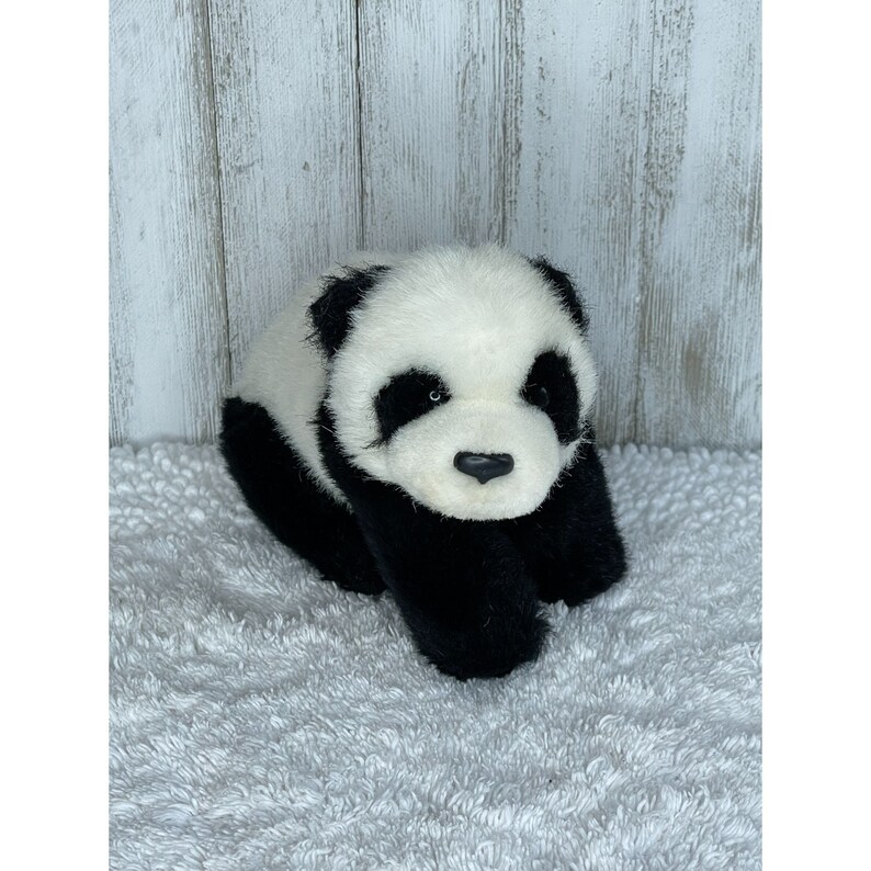 May include: A black and white plush panda bear toy with a soft, furry texture. The panda is lying down with its head tilted slightly to the side. It has black eyes, a black nose, and black paws.