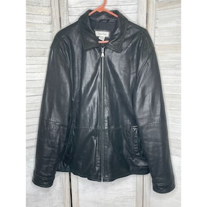 May include: A black leather jacket with a zip-up front and a collar. The jacket has two front pockets and the Calvin Klein logo on the label. The jacket is hanging on a pink hanger.