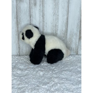 May include: A black and white plush panda bear toy. The panda is sitting on a white fluffy surface.