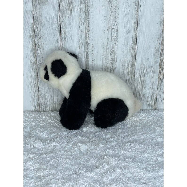May include: A black and white plush panda bear toy. The panda is sitting on a white fluffy surface.