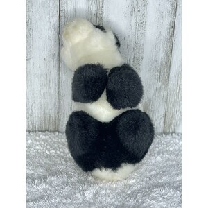 May include: A black and white plush panda bear toy. The panda is sitting up with its back to the camera. The panda has a white face and black ears, eyes, and paws.