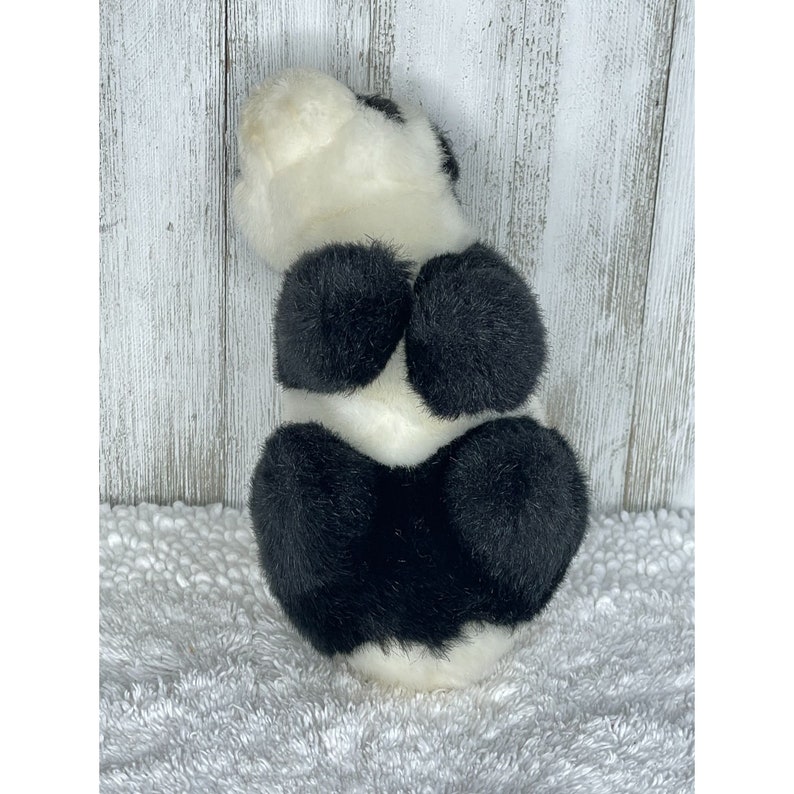 May include: A black and white plush panda bear toy. The panda is sitting up with its back to the camera. The panda has a white face and black ears, eyes, and paws.