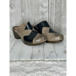 May include: A pair of black and brown leather clogs with a wooden heel. The clogs have a patchwork design and are made of distressed leather.