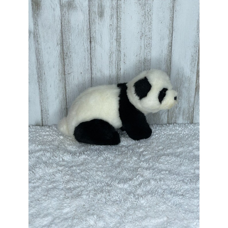 May include: A black and white plush panda bear toy sitting on a white fluffy surface. The panda is lying on its side with its head turned to the right.