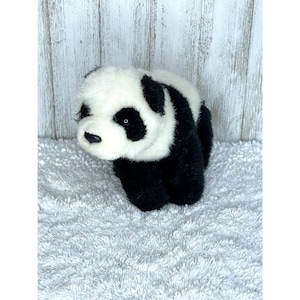 May include: Black and white plush panda bear toy. The panda is sitting on a white fluffy surface.