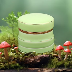 May include: A green ceramic container with a gold trim, sitting on a bed of moss and mushrooms.