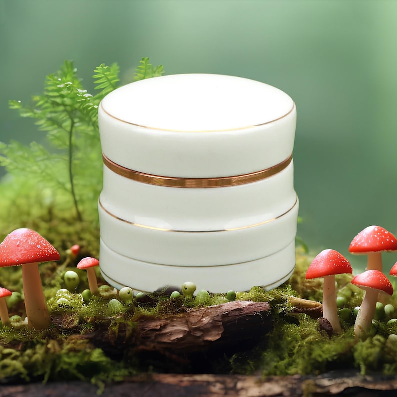 May include: White ceramic jar with gold trim, sitting on a bed of moss and mushrooms.