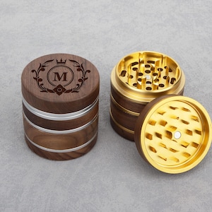 Może przedstawiać: Młynek drewniany z górną częścią wykonaną z metalu w kolorze złotym i srebrnym paskiem. Na górnej części młynka wygrawerowano koronę i literę "M".