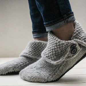 May include: Gray knitted slipper boots with a fold-over cuff and a button closure. The slippers are worn on a person's feet.