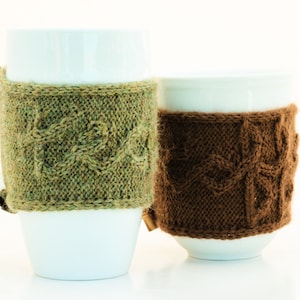 Può includere: Due tazze in ceramica bianca con coperture in maglia. La tazza a sinistra ha una copertura in maglia verde e la tazza a destra ha una copertura in maglia marrone.