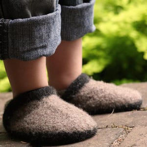 Puede incluir: Un par de zapatillas de lana de punto marrón y negro con textura peluda. Las zapatillas las lleva un niño que lleva unos vaqueros azules remangados.