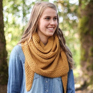 May include: A woman wearing a denim shirt and a mustard yellow knitted shawl. The shawl is a triangular shape with a lacy pattern.