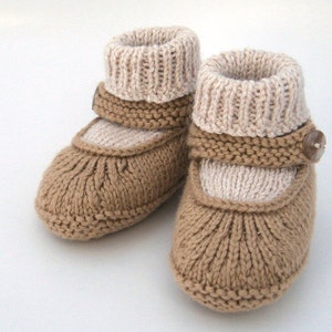 May include: A pair of knitted baby booties in brown and beige with a button detail. The booties have a strap across the top and a fold-over cuff.