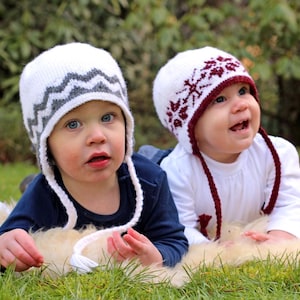 Può includere: Due bambini indossano cappelli di lana bianca con motivi colorati. Il bambino a sinistra indossa un cappello grigio e bianco con un motivo a chevron. Il bambino a destra indossa un cappello rosso e bianco con un motivo a fiocco di neve. Entrambi i bambini sorridono.