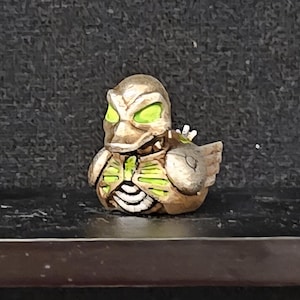 May include: A white ceramic mug with a black handle and the text "But First, Coffee" in a bold, black font. The mug is set against a blurred background, suggesting a cozy setting. The mug appears to be approximately 4 inches tall.