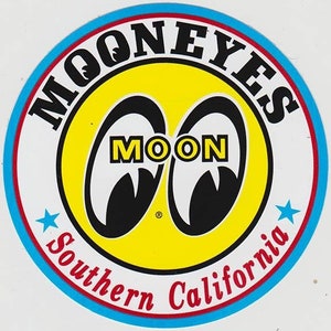 May include: A white circle with a blue and red border. Inside the circle is a yellow circle with two black eyes that say "MOON" in white letters. The text "MOONEYES" is written in black letters around the yellow circle. The text "Southern California" is written in red letters around the bottom of the circle.