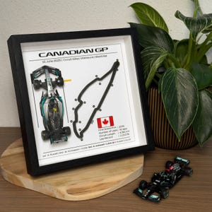 Könnte beinhalten: Gerahmter Druck der kanadischen Grand-Prix-Strecke mit schwarz-weißem Streckenlayout, einer Rennwagenillustration und dem Text "CANADIAN GP". Ein Miniatur-Rennwagen ist ebenfalls vorhanden. Der Rahmen ist schwarz.