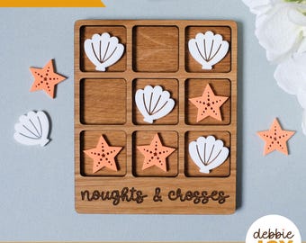 May include: A wooden game board with a grid of nine squares. The board is decorated with a seashell and starfish design. The words "noughts & crosses" are engraved on the board. The game is designed for children to play.