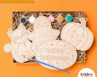 May include: A Halloween-themed craft kit with wooden cutouts of a cat, ghost, and pumpkin, along with paint pots and a paintbrush. The oval cutout says "Happy Halloween". The words "Laser tested" and "SVG laser ready files | Digital download" are also visible.